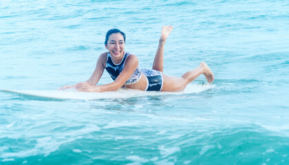 Asian women wearing swimsuits hobby happy fun lying surfing waves on board in the sea is an...