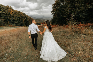 Wedding couple walks in the mountains. The groom leads the bride by the hand. The dress of the bride develops in the wind.