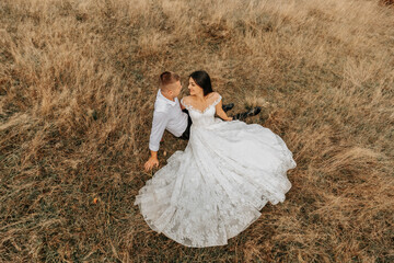 The bride and groom are lying on the dry grass and hugging, a woman in a white wedding dress. Beautiful autumn wedding photo.