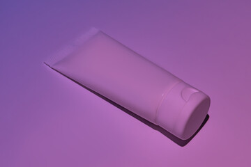 Unbranded white squeeze cosmetic cream bottle tube on neon pink background. Natural oranic spa cosmetics concept. Mockup, template