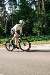 Professional cyclist in sports equipment trains on a road bike outside the city, rides on the road against the background of the forest.