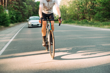 A cyclist in gear rides along an asphalt road outside the city together with cars.