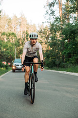 A male cyclist rides on the road for cars on a road bike outside the city on the background of the forest.