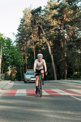 Fototapeta premium Positive young male cyclist riding a road bike on an asphalt road outside the city and smiling. Vertical photo.