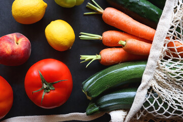 Mesh bag with fresh seasonal fruit and vegetable. Top view, dark background.