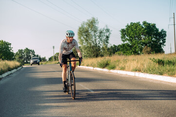 A sporty active man in gear walks on a road bike outside the city on roads for cars.