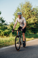Obraz premium Photo of a male professional cyclist in sports equipment riding a road bike outside the city on an asphalt road. Vertical