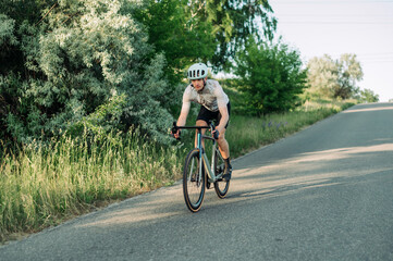 Fototapeta na wymiar Male professional sportsman cyclist training on a road bike outside the city on an asphalt road, riding downhill