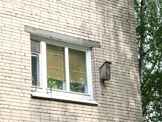 A small wooden homemade birdhouse on the wall of a residential building near the window
