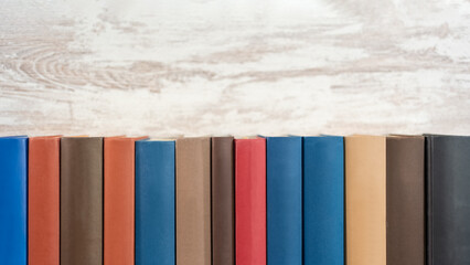 Book backs of different colors neat with a wooden background. Photo with copyspace.