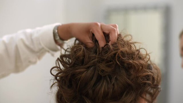 Close-up hands of unrecognizable female hairdresser carefully puts strands of hair using bobby pins in modern beauty studio. Hairstylist giving beauty salon service and treatment to beautiful customer