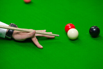 Snooker shot. Closeup view of cue, fingers, white, black and red ball before shot