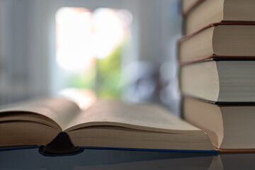 Fototapeta premium Books stacked next to an open book with a flash of light in the background. Photo with copyspace.
