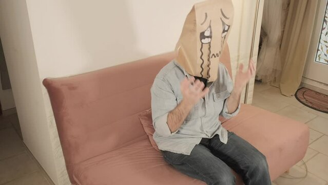 A man wearing a breadbag face, sitting on the couch at home, crying desperate rivers of tears.
