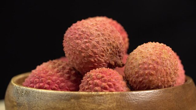 Fresh lychee fruit in shell rotate in wooden bowl in macro on black background. Lychee berries for making lemonade and refreshing drink