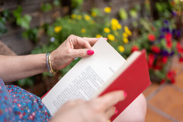 Woman reading a book in the garden with plants with flowers of different colors.