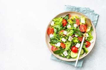 Green salad with spinach, arugula, tomatoes and feta with olive oil. Top view on white.
