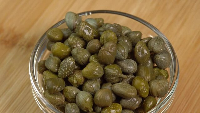 Pickled marinated capers rotate in glass bowl in macro. Ingredients for making spicy sauce, tartare or salad