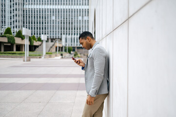 Man using smartphone leaning against wall