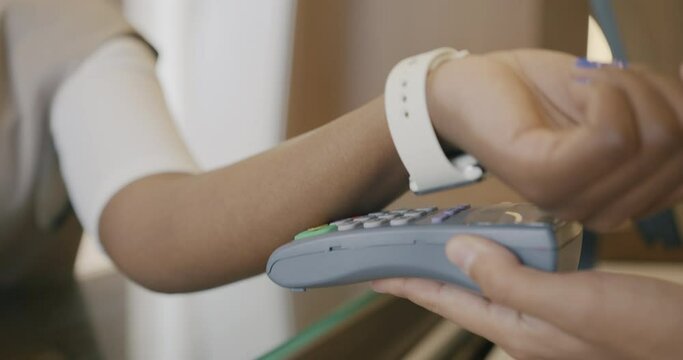 Close-up of female hand wearing smart watch making cashless payment in hotel lobby while business lady is checking-in. People and modern technology concept.