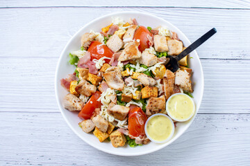 Bowl salad with pieces of roasted pork, grated cheese, beans, corn, tomato, nachos, lettuce, with house mayonnaise