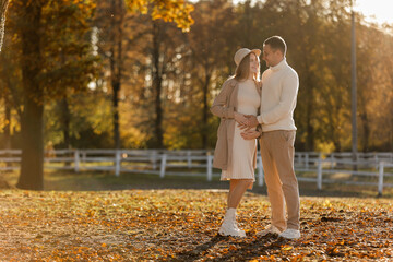 Fototapeta premium Young stylish couple lovers are hugging and kissing in the autumn park. Lovely romantic moment between man and woman in love, looking to each others. Happy family. Love, youth, happiness concept.