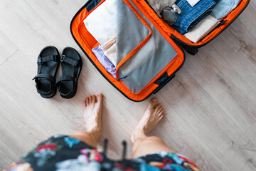 A young man is packing clothes in a suitcase in his apartment for the summer holidays. The luggage...
