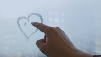 Female hand drawing doodle smile face heart on glass wet blue window at home - Powered by Adobe