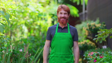 Naklejka na ściany i meble One happy young male gardener wearing Green Apron with arms crossed smiling at camera in natural garden environment