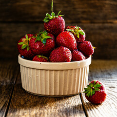 Ripe tasty strawberries in a ceramic bowl on a wooden table.