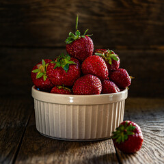 Ripe tasty strawberries in a ceramic bowl on a wooden table.
