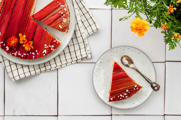 Rhubarb cake with geometric pattern and marigold flowers as a decoration on a white tiles. Spring and summer sweet-sour healthy dessert. Top view