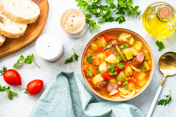 Minestrone soup, italian vegetable soup with smoked sausages, Top view on white table.