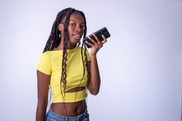 Mujer hermosa joven de color que usa el teléfono inteligente  en una fondo blanco. Chica estudiante sonriente enviando mensajes de voz en el teléfono móvil.. - obrazy, fototapety, plakaty