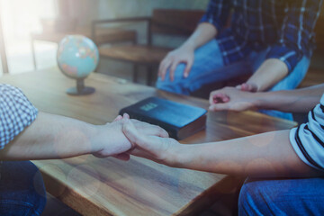 Close up of a small group of christian friends holding hand and pray together wirh blur holy bible and world globe on wooden table, world missing concept