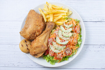 Bowl of two pieces of roasted chicken, accompanied by lettuce, tomato, cucumber, French fries and Parmesan cheese