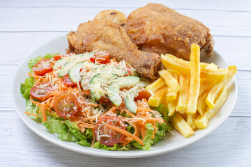 Bowl of two pieces of roasted chicken, accompanied by lettuce, tomato, cucumber, French fries and Parmesan cheese