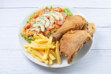 Bowl of two pieces of roasted chicken, accompanied by lettuce, tomato, cucumber, French fries and Parmesan cheese