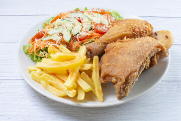 Bowl of two pieces of roasted chicken, accompanied by lettuce, tomato, cucumber, French fries and Parmesan cheese