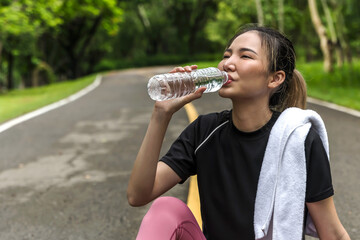 Asian sport woman sitting and drinking water from bottle relax after jogging in park, Woman Workout in park