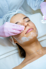 Beautician's hands cleaning female face with cotton pads at aesthetic clinic.