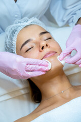 Beautician doctor cleaning woman face with cotton pads, skin care procedures, rejuvenation.
