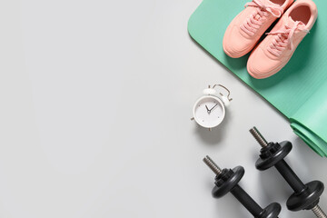 Sport and fitness equipment, female pink shoes, timer, dumbbells, yoga mat on gray background. View from above. Copy space.
