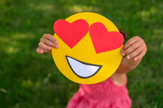 A close-up of the face of a lover smile with eyes in the shape of red hearts in the hands of a person.