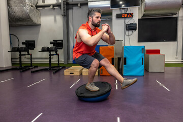 Fit athletic man performing exercise on gymnastic hemisphere bosu ball in gym.