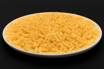 Uncooked Fusilli Pasta Lying on White Plate on Black Background. Raw and Dry Macaroni. Unhealthy and Fat Food