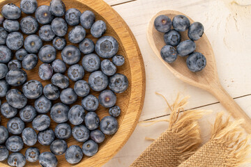 Several sweet blueberries with round wooden tray and wooden spoon on wooden table, macro, top view.