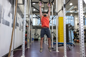 Fototapeta na wymiar Fit man pulling up on gymnastic rings in gym, training, training his biceps and triceps.