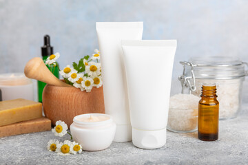 Chamomile Spa. Essential oil, sea salt, chamomile flowers, body cream and handmade soap. Natural herbal cosmetics with chamomile flowers on a textured background.Beauty concept. Cosmetic tube. 