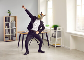 Man in suit and funny animal mask having fun at end of work day. Happy lazy irresponsible guy dancing in office wearing unusual bizarre silly wacky rubber donkey mask in glasses. Weekend party concept - obrazy, fototapety, plakaty